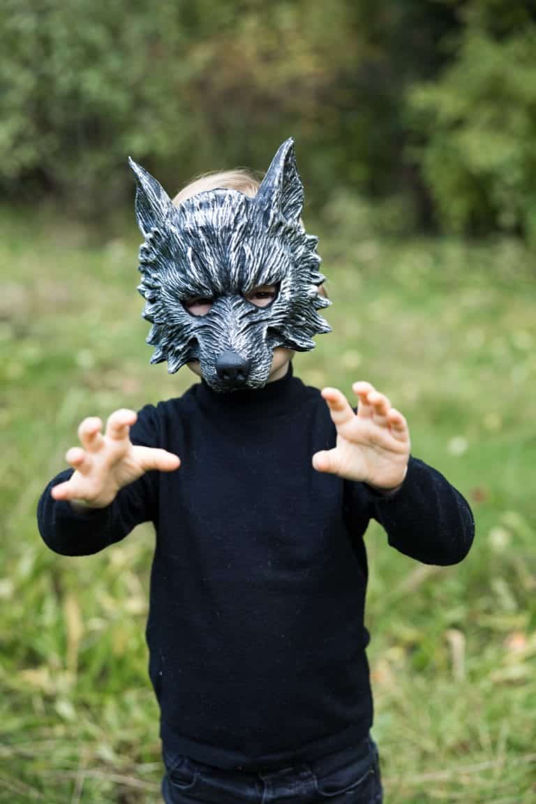 Kind in zwart shirt draagt een grijs weerwolfmasker met puntige oren en houdt de handen als klauwen voor zich