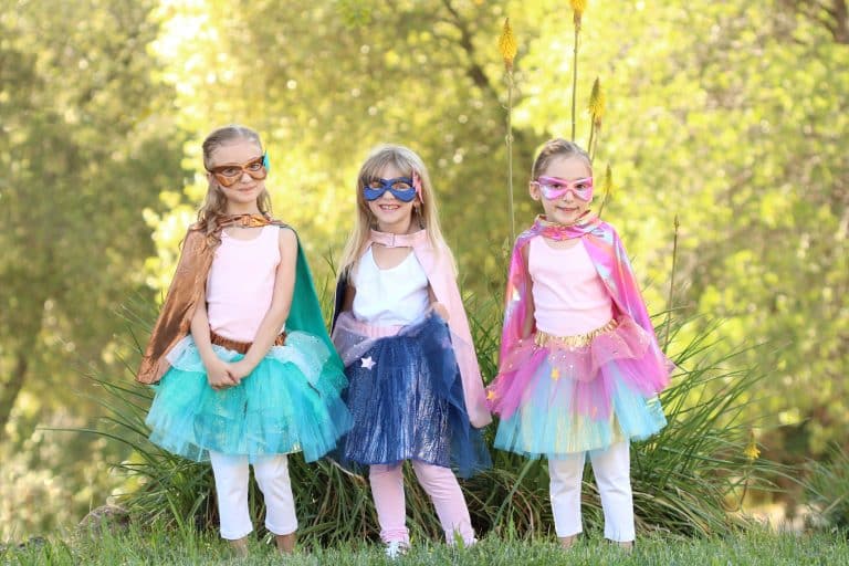 Links draagt een meisje de mintgroene superhelden verkleedset met tutu, cape superheld en masker; twee meisjes staan ernaast.