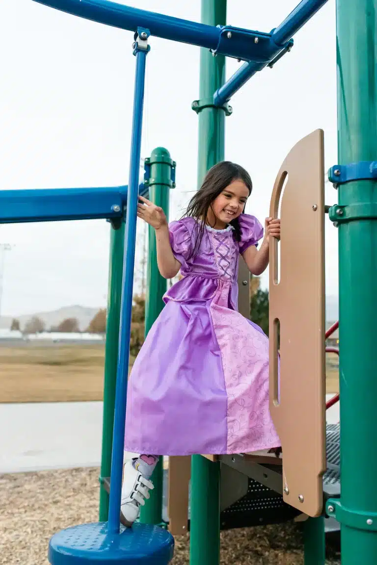 Meisje draagt een paarse Rapunzel prinsessenjurk van Little Adventures tijdens het klimmen op een speeltoestel