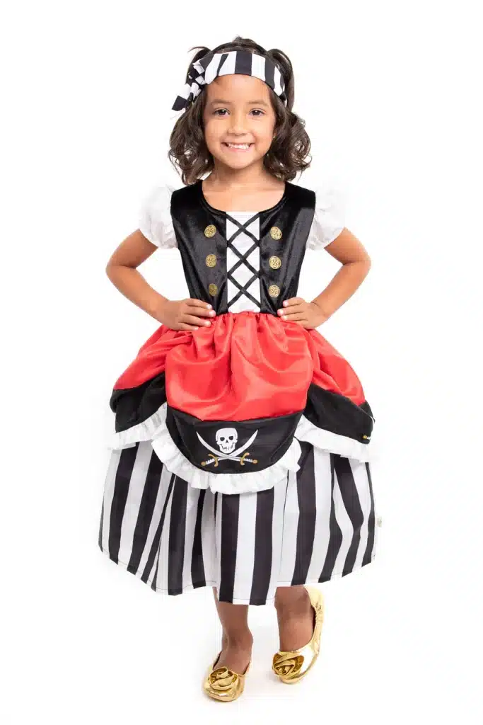Meisje draagt de Little Adventures piraten prinsessenjurk met zwart-witte strepen, rode rok, doodshoofd en bijpassende hoofdband.