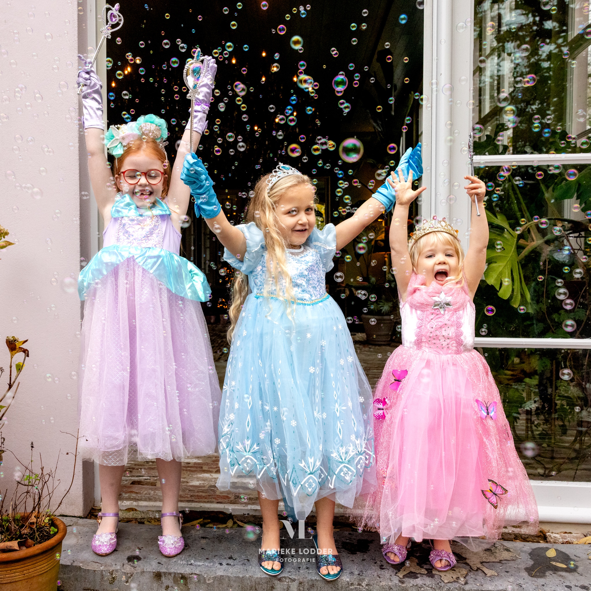 Drie meisjes dragen een paarse Ariël jurk, blauwe Elsa jurk en roze Doornroosje jurk bij een bellenblaasactie.