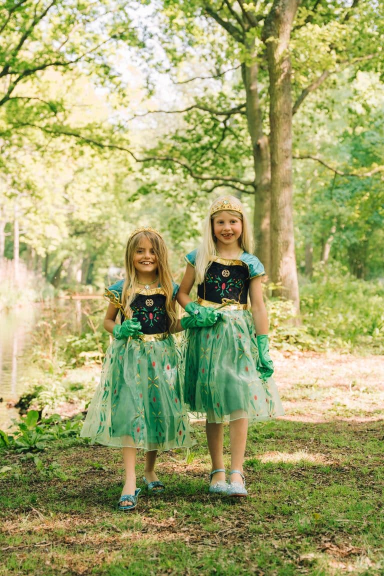 Twee meisjes dragen groene Anna-prinsessenjurken uit het Frozen Anna-prinsessenpakket, met handschoenen en kroontjes in het bos.