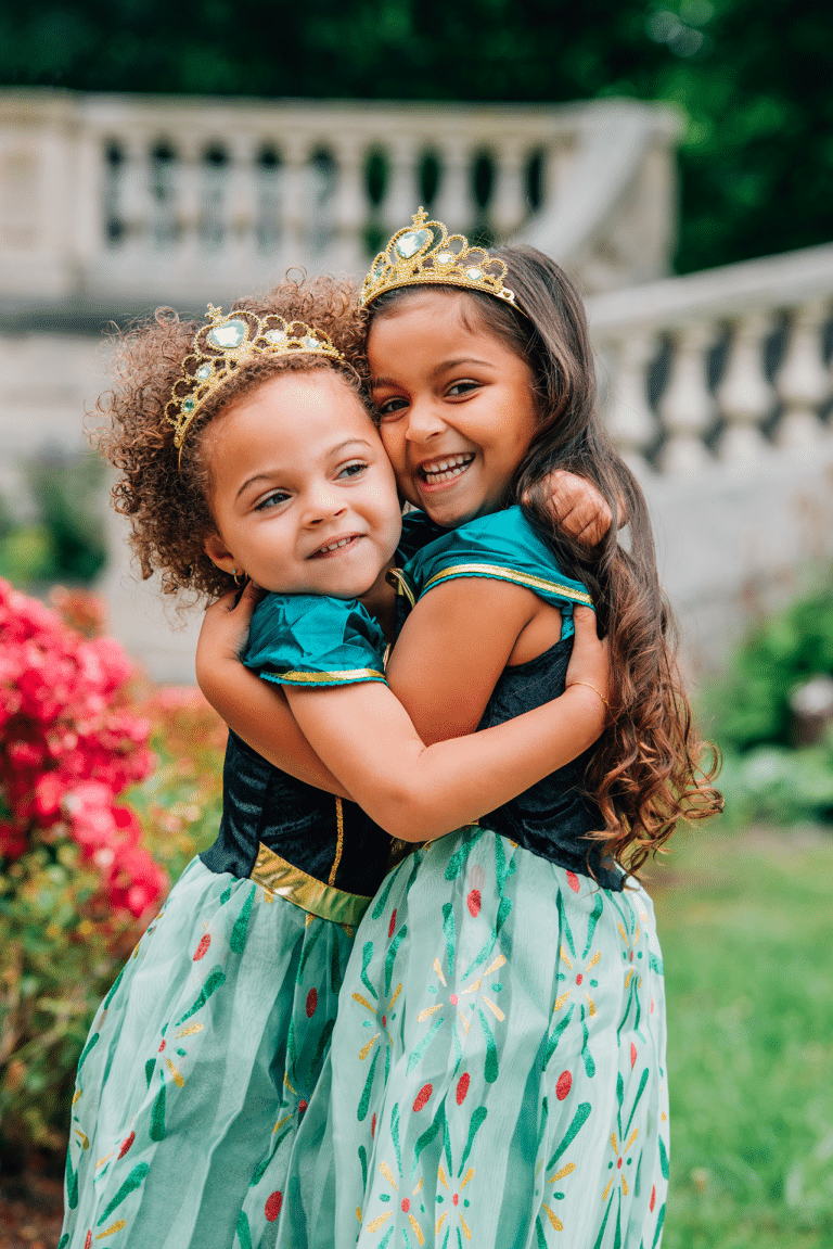Combideal van Het Betere Merk: twee meisjes dragen de Anna en Elsa jurk met gouden kroontjes en groenblauwe rokken in een tuin.