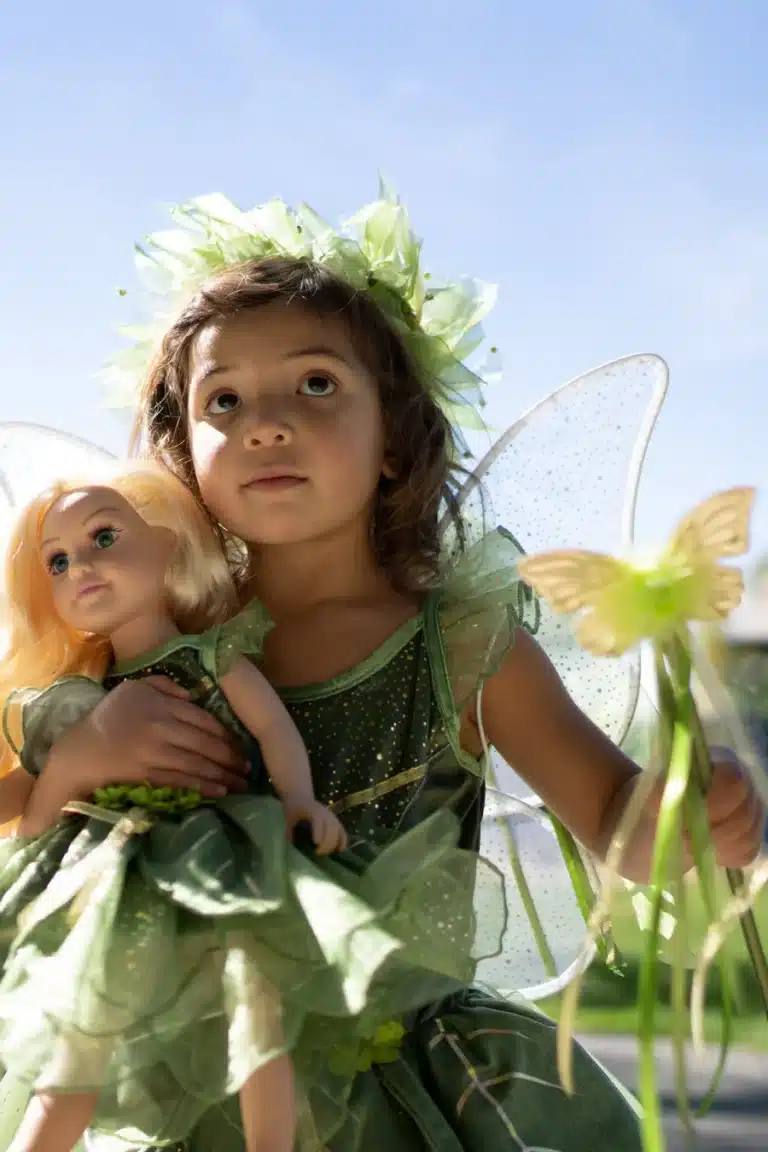 Meisje draagt de groene Tinkerbell-bloemenkrans en feeënvleugels en houdt de bijpassende toverstaf vast