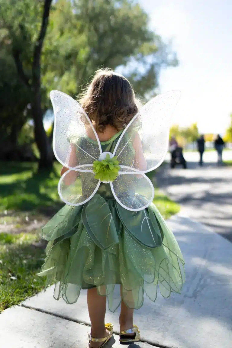 Een kind draagt groene vleugels met glitters en een bloem over een groen elfjeskostuum, gezien van achteren.