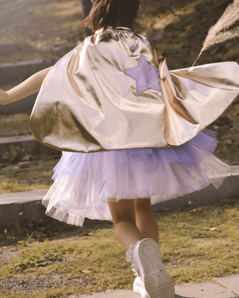 Meisje draagt een glanzende prinsessen cape met paarse ster en wijde mouwen, boven een paarse tule rok