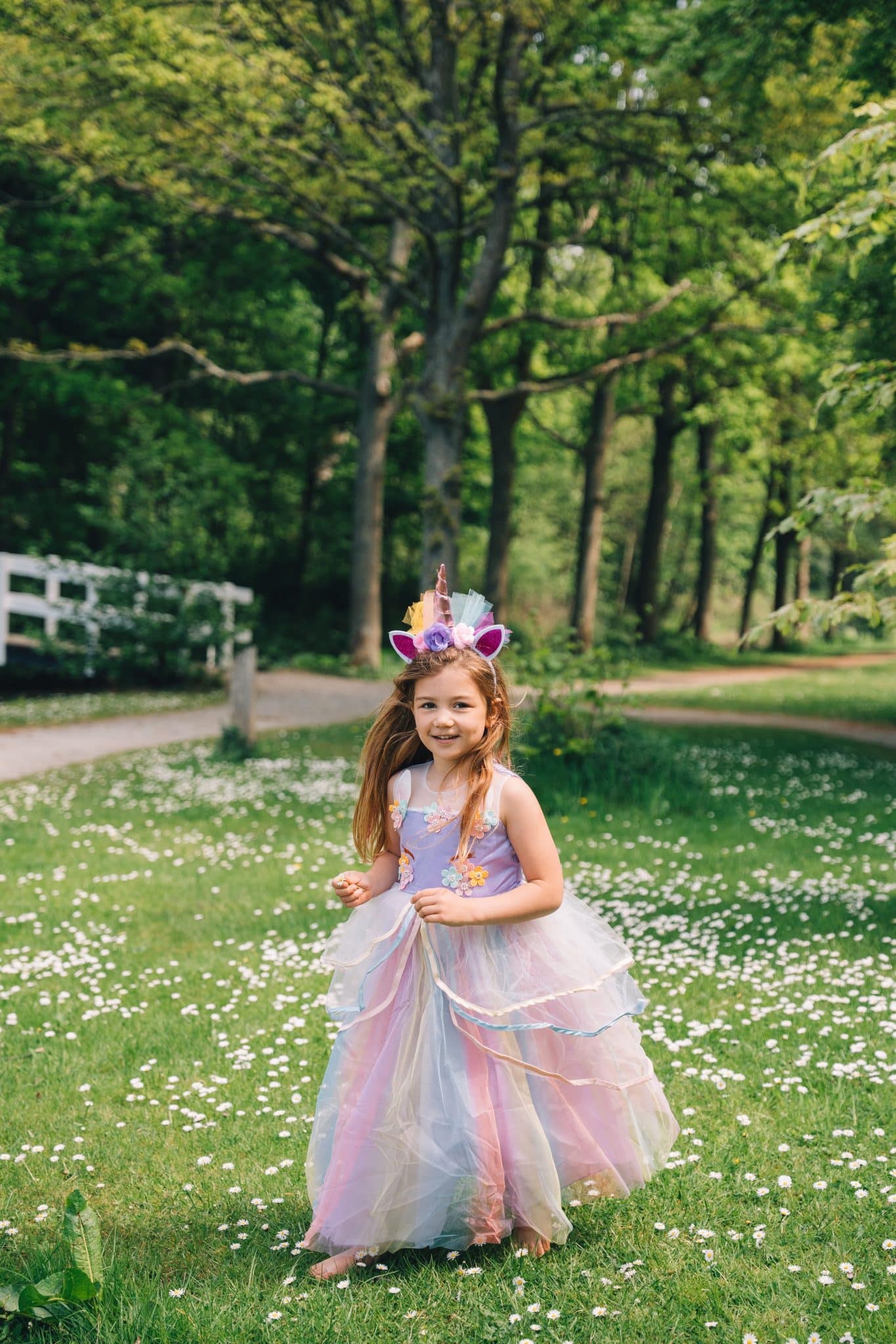 Meisje draagt een lila unicorn jurk met tule rok en bijpassende haarband in een bloemrijke tuin.