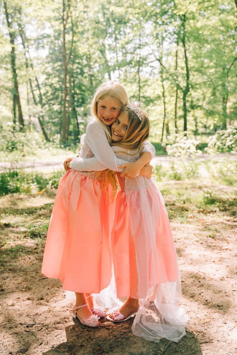 Twee meisjes dragen roze Elsa-jurken; de prinsessenjurk met lange mouwen heeft een glanzende rok in het bos.
