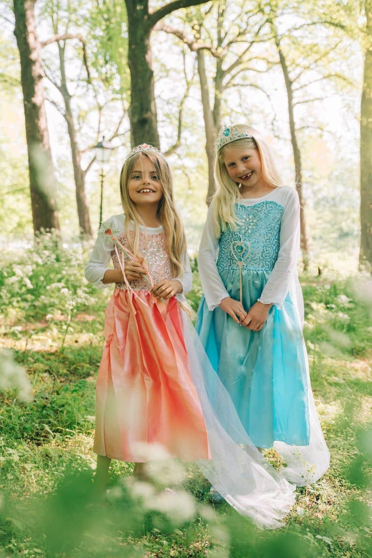 Twee meisjes dragen een roze Rapunzel- en blauwe Elsa-prinsessenjurk met lange mouwen in een bos.