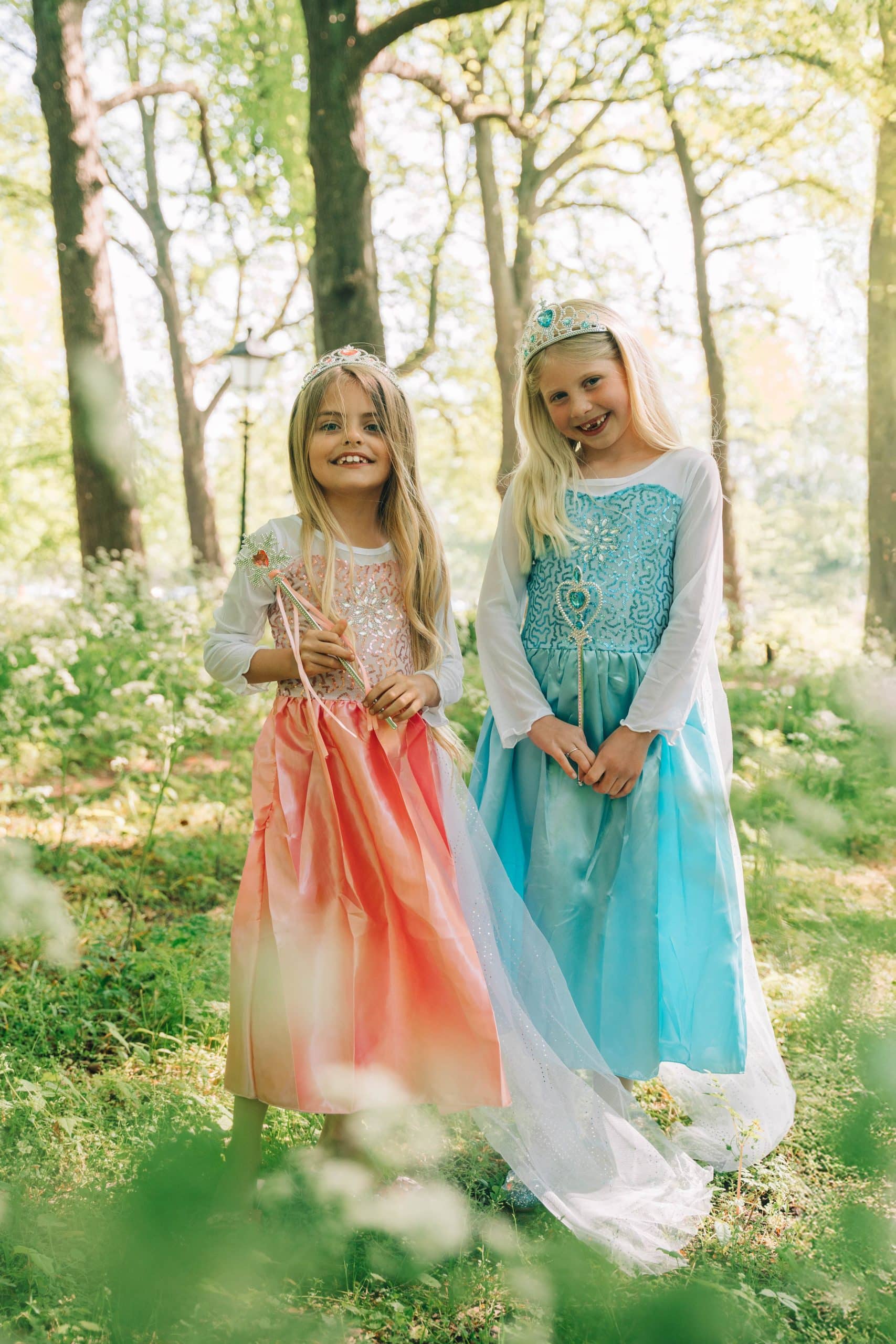 Twee meisjes dragen een roze Rapunzel- en blauwe Elsa-prinsessenjurk met lange mouwen in een bos.