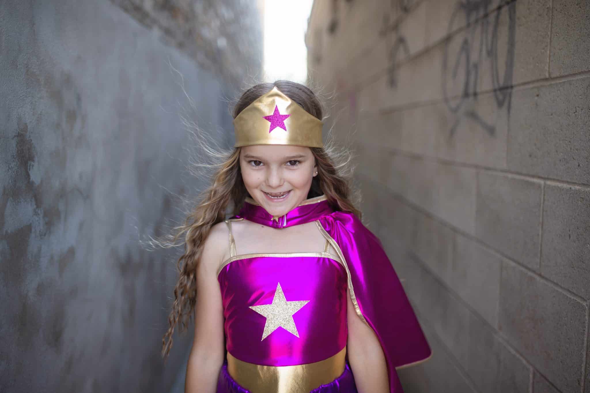 Meisje draagt het paarse superhelden verkleedkostuum met gouden hoofdband en grote ster op het topje.