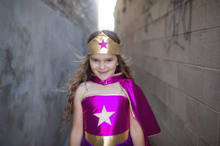 Meisje draagt het paarse superhelden verkleedkostuum met gouden hoofdband en grote ster op het topje.