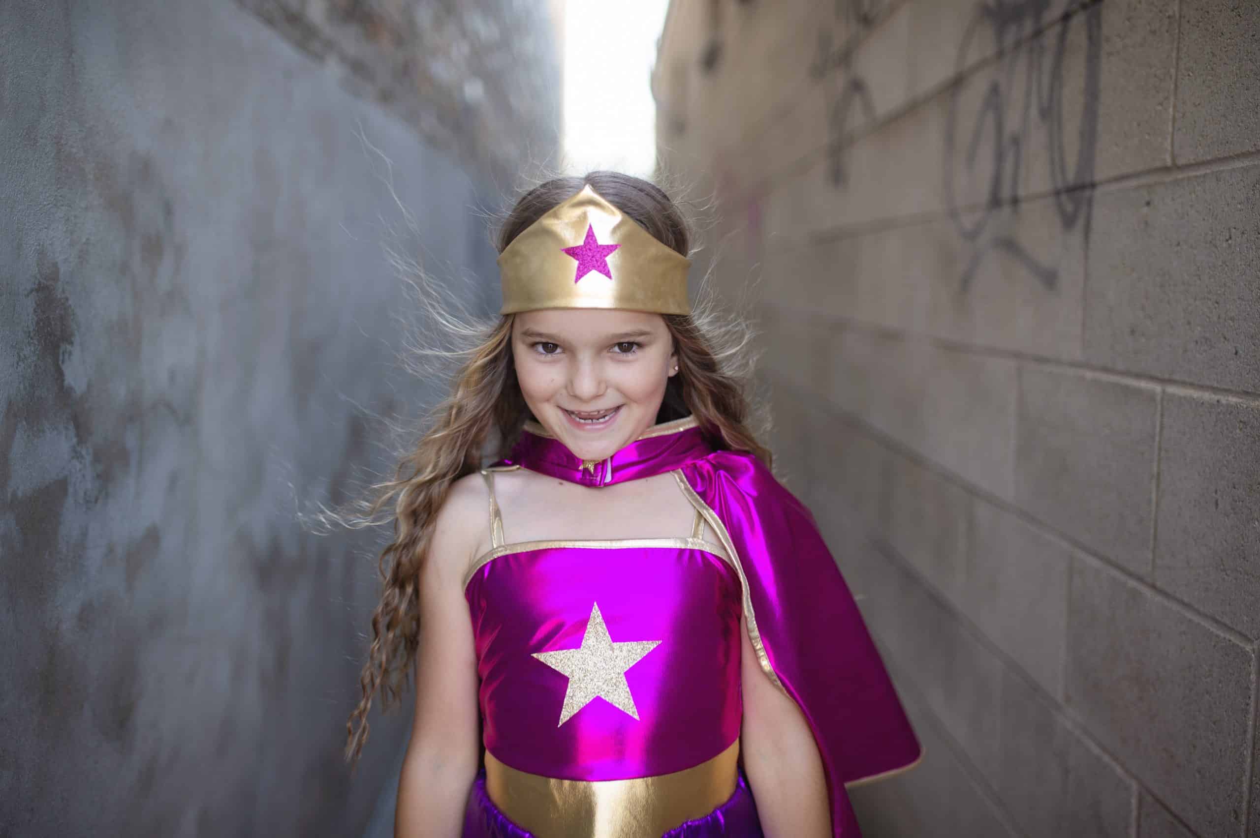 Meisje draagt het paarse superhelden verkleedkostuum met gouden hoofdband en grote ster op het topje.