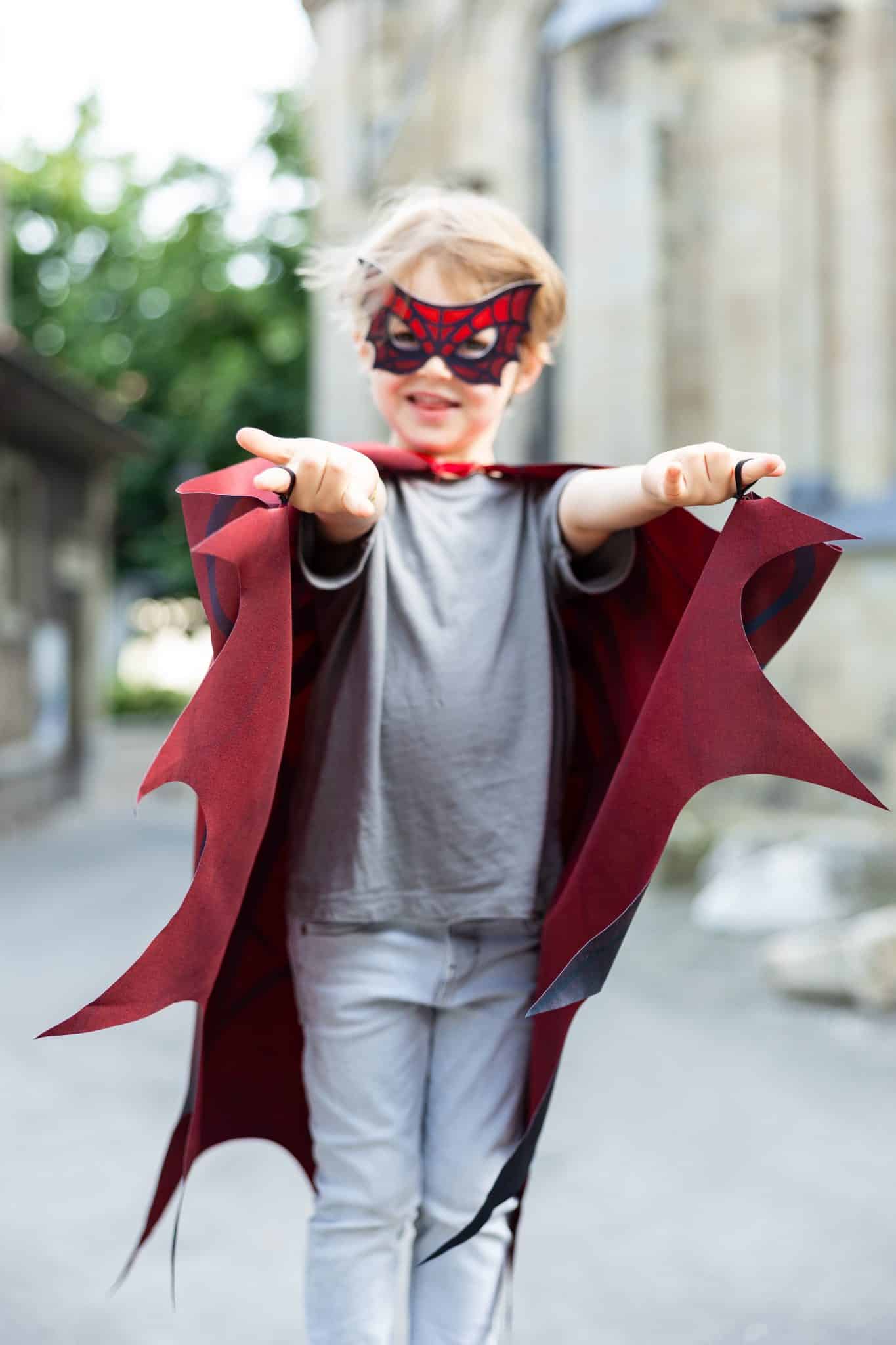 Jongen draagt een rode spiderman cape met bijpassend masker en houdt de vleugels uitgespreid