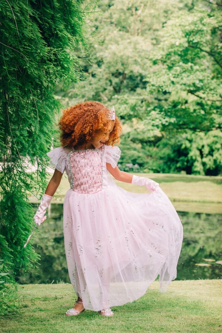 Meisje draagt een roze Elsa-prinsessenjurk met handschoenen en toverstaf in een groene tuin