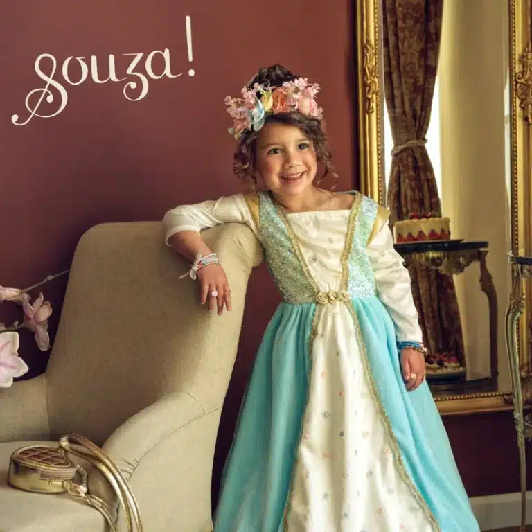 Meisje draagt de Souza! Josephina blauwe prinsessenjurk met witte mouwen, gouden randen en een lichtblauwe rok in een woonkamer.
