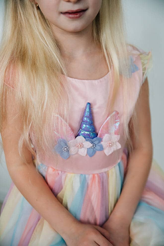Detail van een meisje in een roze unicorn jurk met glanzende hoorn, bloemen op het lijfje en pastelkleurige tule rok