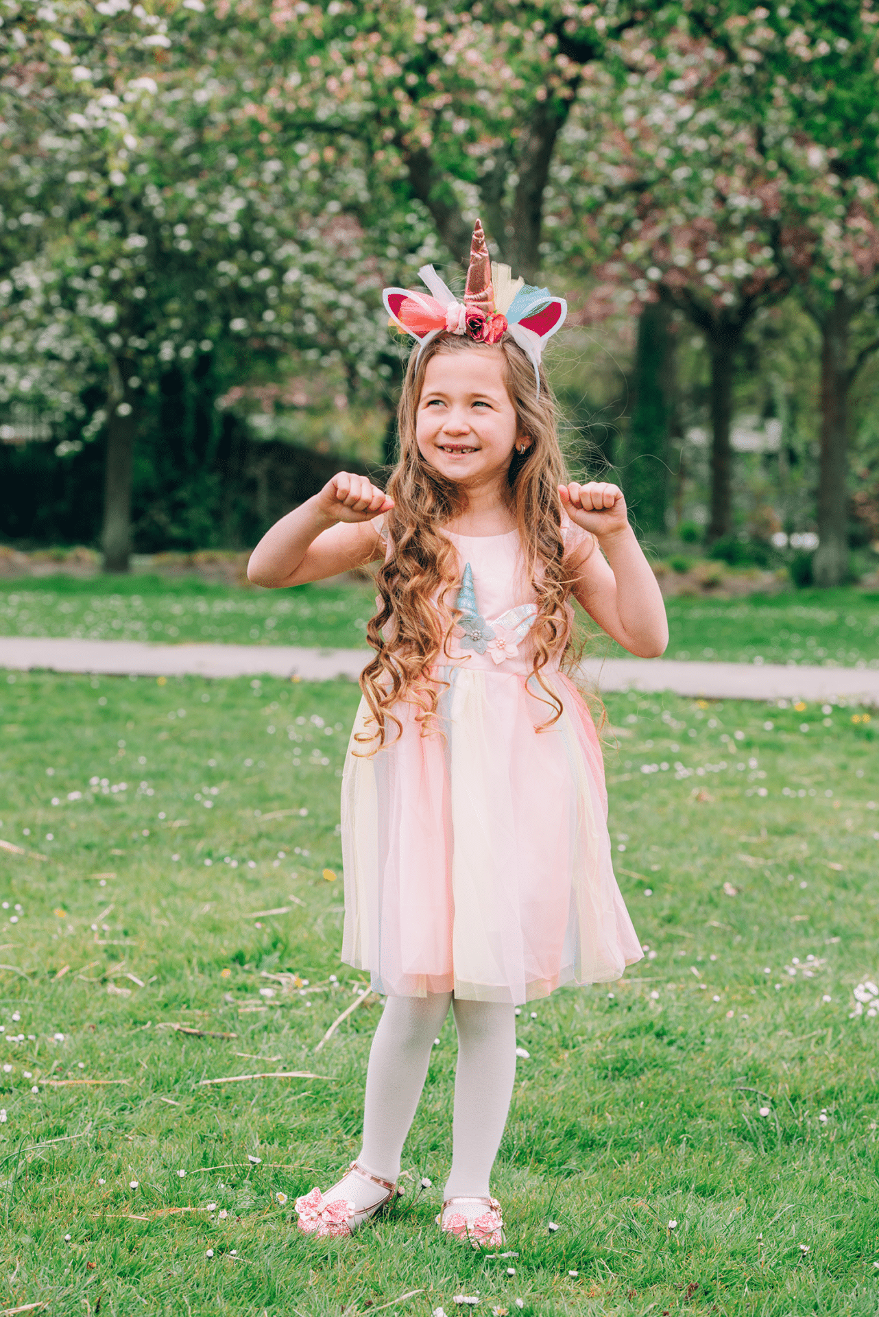 Meisje draagt een roze unicorn prinsessenjurk met tule rok en bijpassende eenhoornhaarband in het park.