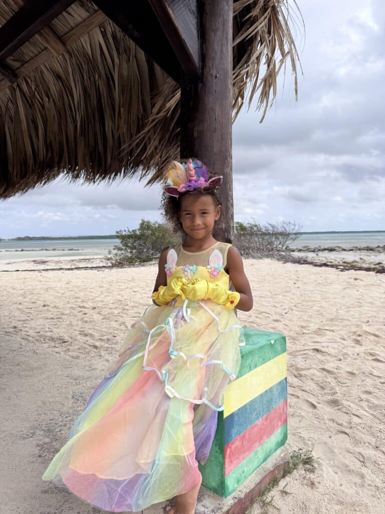 Meisje draagt een gele unicorn jurk met kleurrijke tule rok, gele handschoenen en eenhoornhaarband op het strand