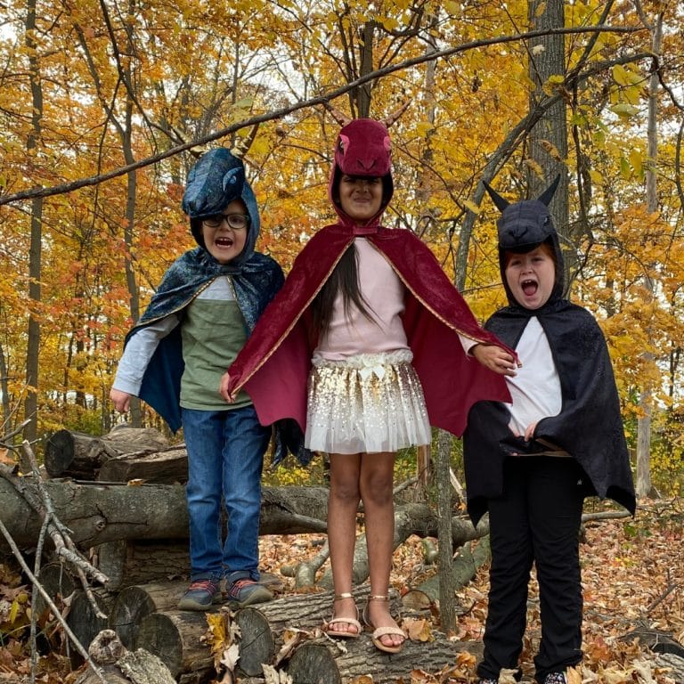 Meisje draagt een rode drakencape met capuchon tussen twee kinderen in dierenkostuums in een herfstbos