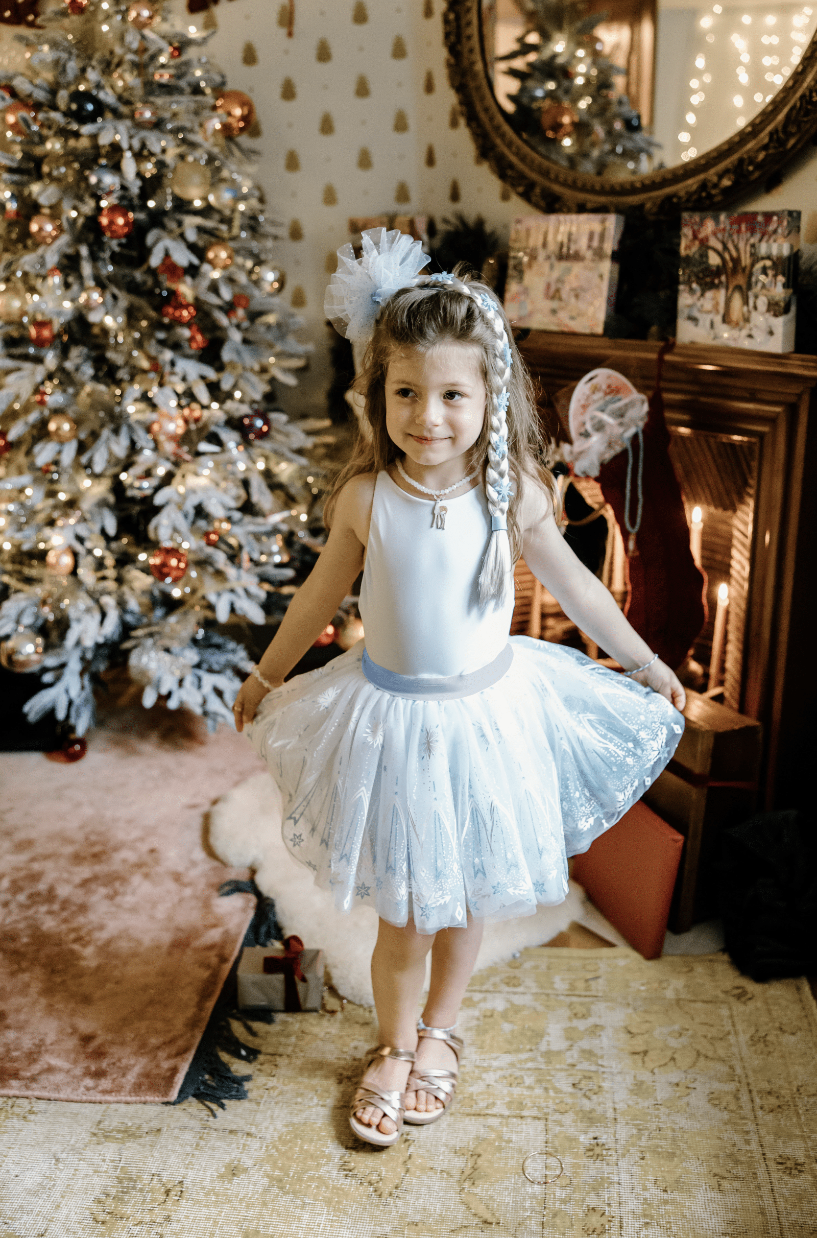 Meisje draagt de Great Pretenders witte tutu rok met glanzende sterrenprint naast een versierde kerstboom.
