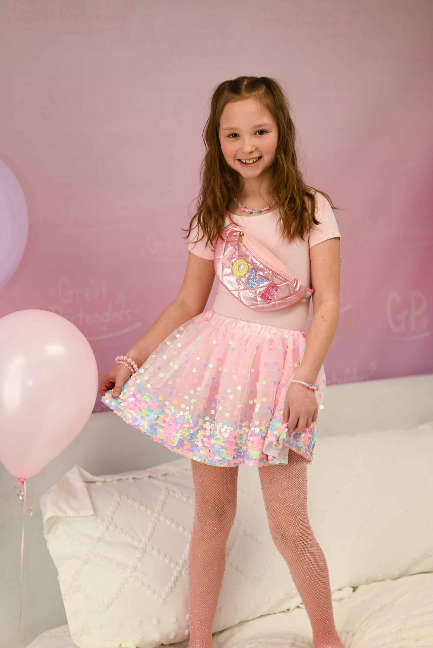 Meisje draagt de Great Pretenders roze pailletten rok met iriserende glansrand en roze panty, naast een roze ballon.