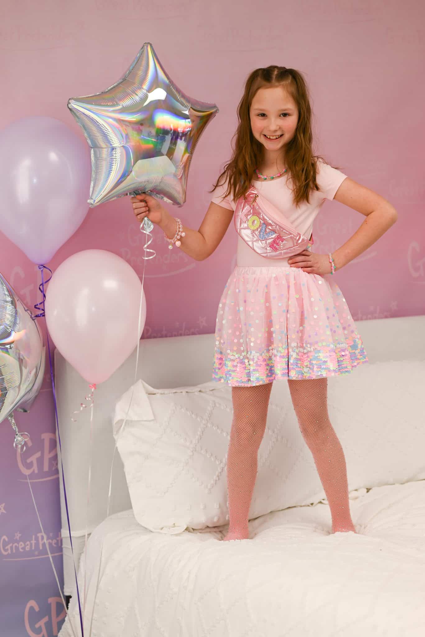 Meisje draagt de roze paillettenrok met kleurrijke glansrand en tule, terwijl ze een sterballon vasthoudt