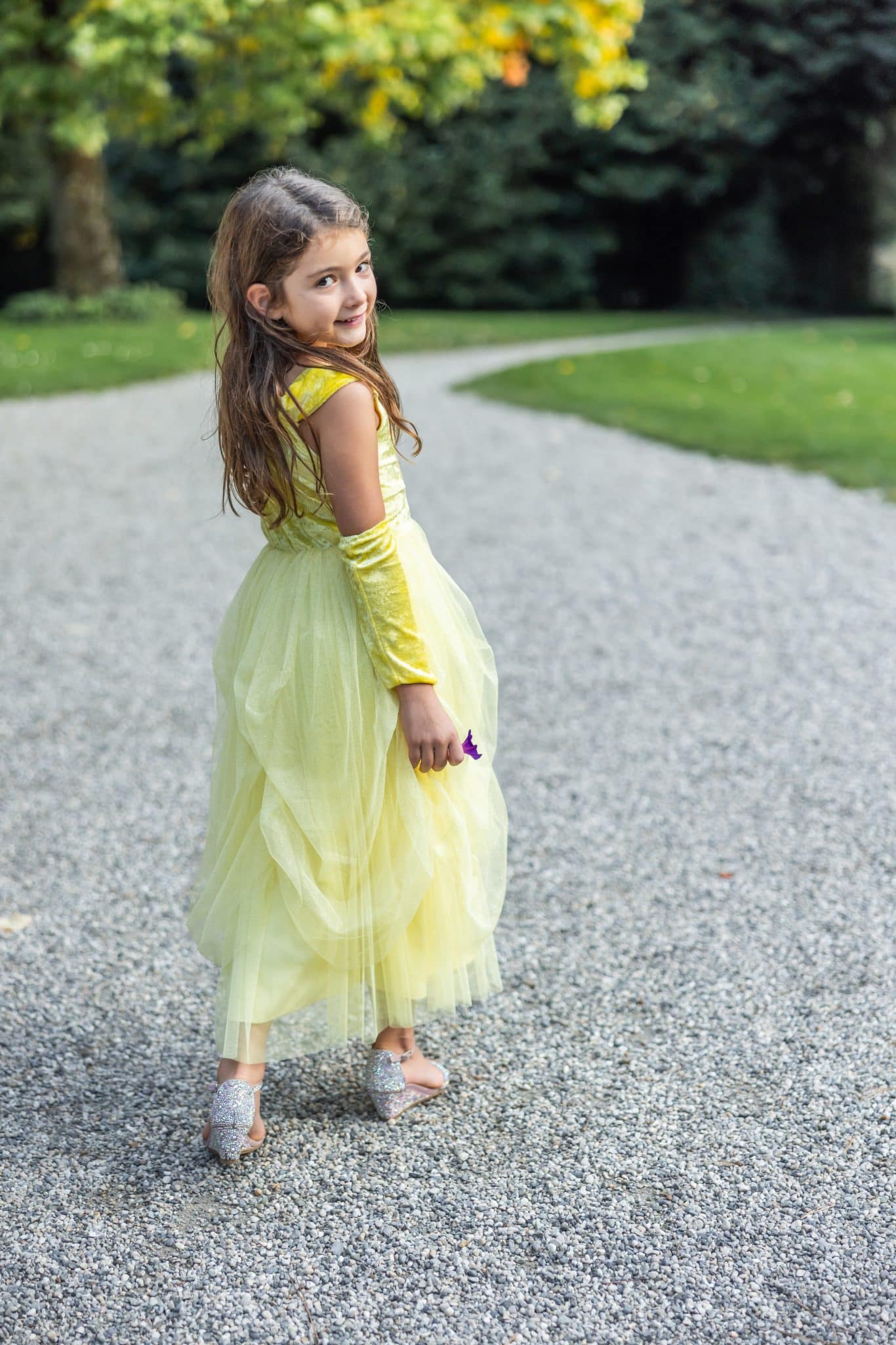 Meisje draagt buiten de gele Belle-jurk van Great Pretenders met lange handschoenen en een volle tule rok.