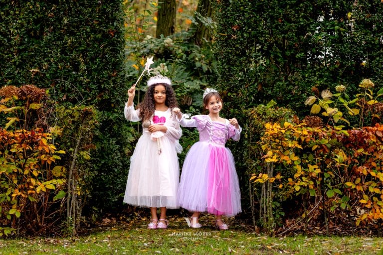 Twee meisjes dragen verkleedkleren uit de combideal: een witte elfjesjurk en een paarse Rapunzel jurk in een herfstige tuin.