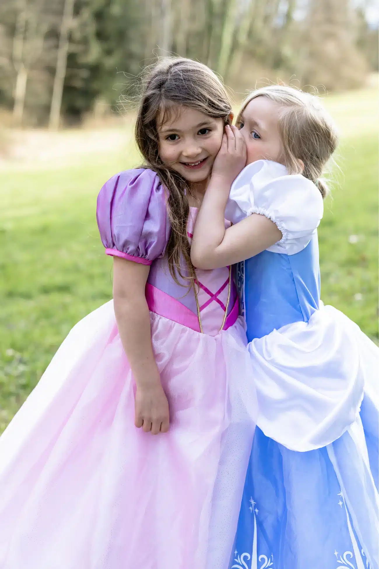 Meisje draagt een paarse Rapunzel prinsessenjurk met roze tule rok naast een meisje in een blauwe prinsessenjurk buiten.
