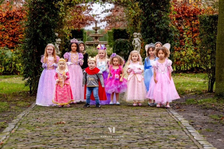 Kinderen dragen sprookjesjurken in verschillende kleuren, waaronder een roze prinsessenjurk, in een herfstige tuin.