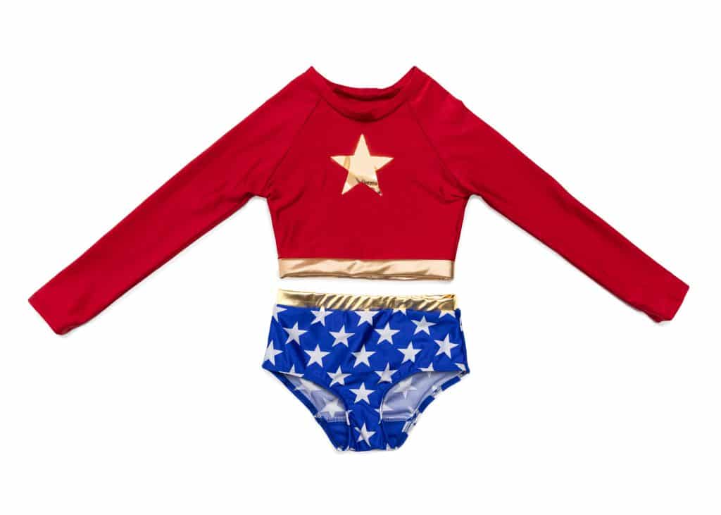 Op een witte achtergrond ligt het Super Girl badpakje met rode top, gouden ster, lange mouwen en blauwe onderkant met witte sterren.