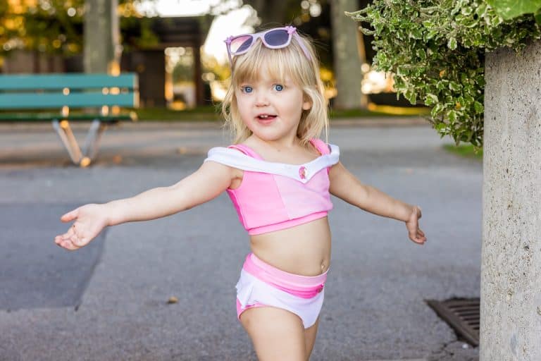 Meisje draagt het roze Doornroosje zwempakje in bikini-stijl met witte schouderbanden en volantrokje