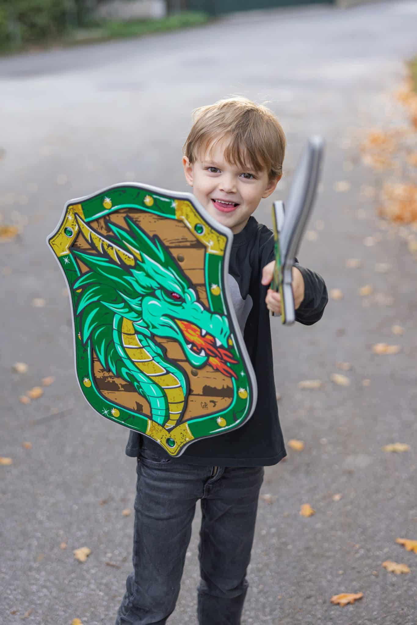 Jongen houdt een groen Great Pretenders ridder schild met draak en een zilverkleurig drakenzwaard vast.