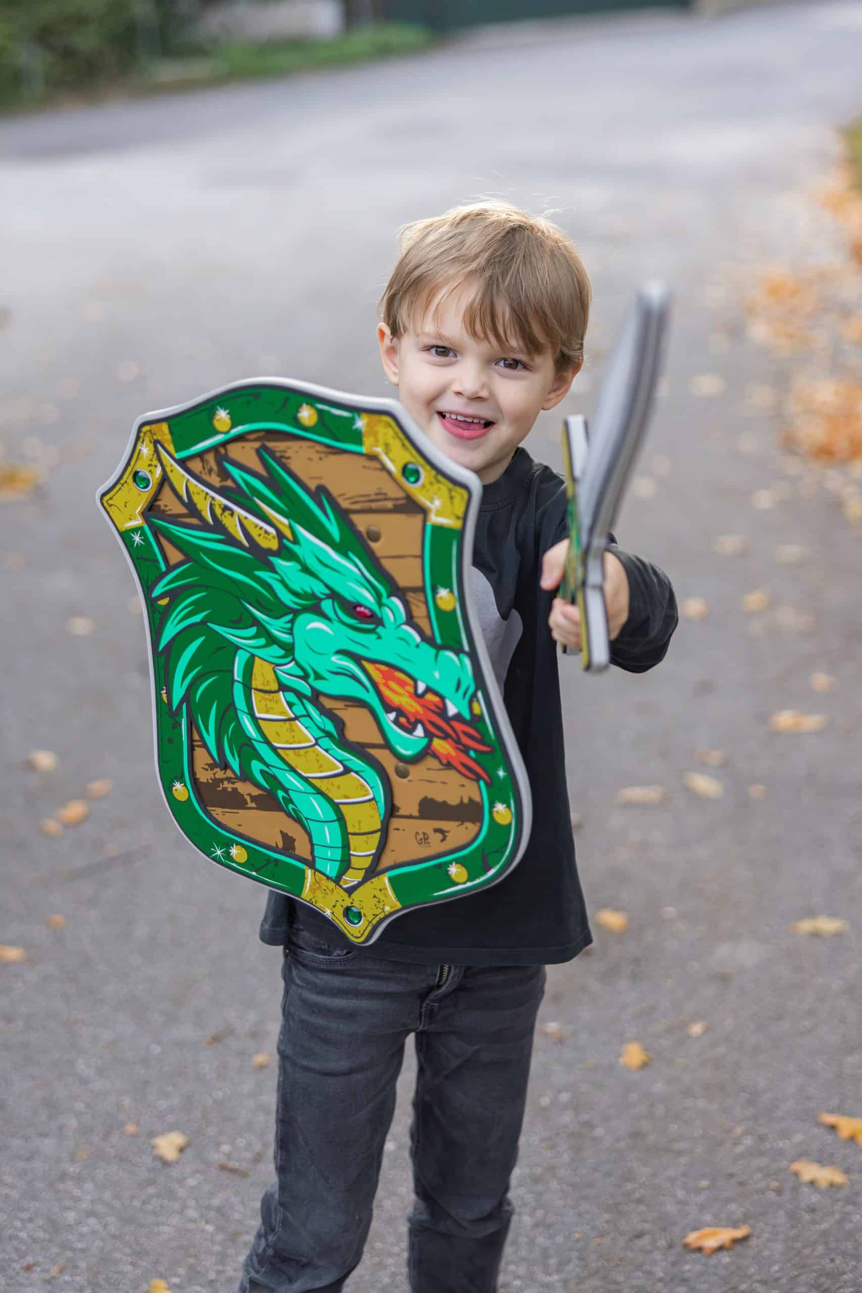Jongen houdt een groen Great Pretenders ridder schild met draak en een zilverkleurig drakenzwaard vast.