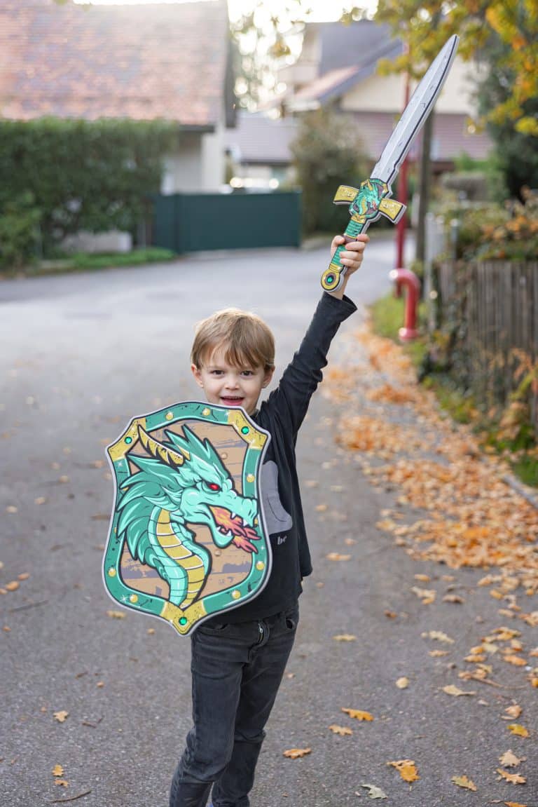 Jongen houdt het ridder-draken zwaard omhoog en draagt een ridders schild met een groene draak.