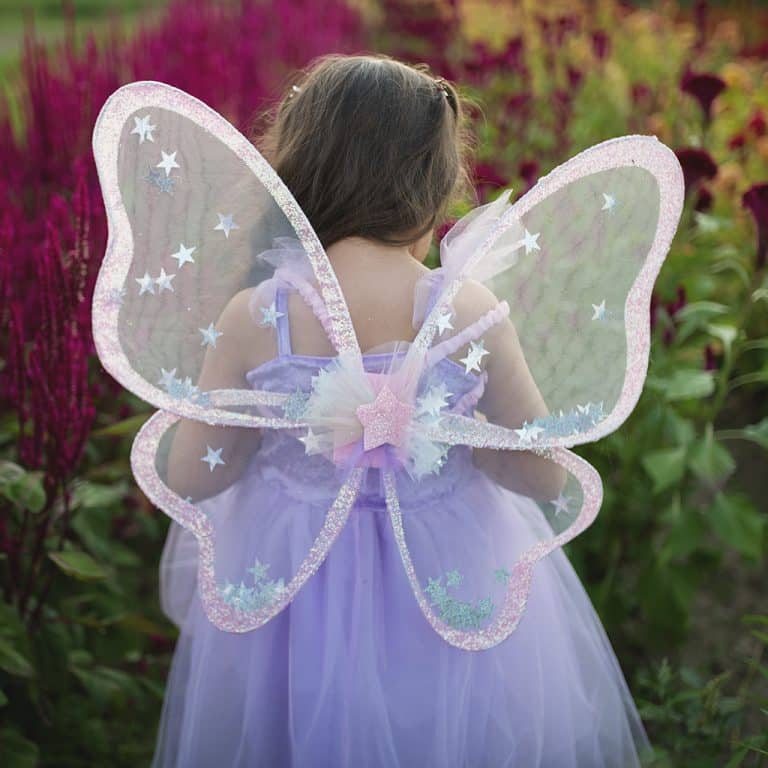 Een kind draagt de vleugels van starfee van Great Pretenders, met pastelkleuren en witte sterren in een groene tuin