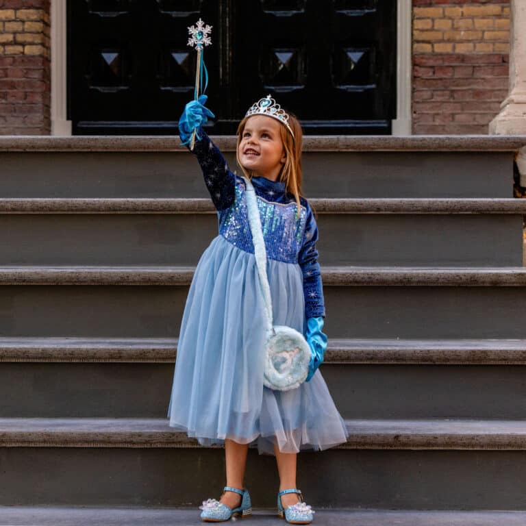 Meisje draagt een blauwe prinsessenjurk elsa met glinsterend lijfje, tiara, handschoenen en toverstaf op de trap.