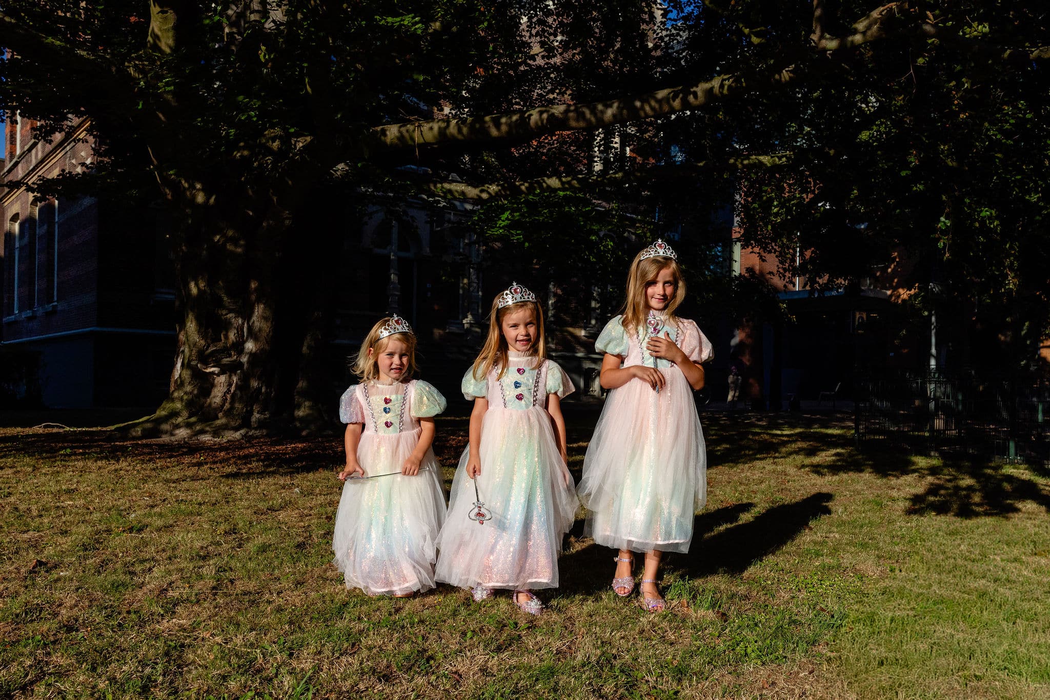 Drie meisjes dragen een regenboog prinsessenjurk met kroon en zachte tule rokken in het park.