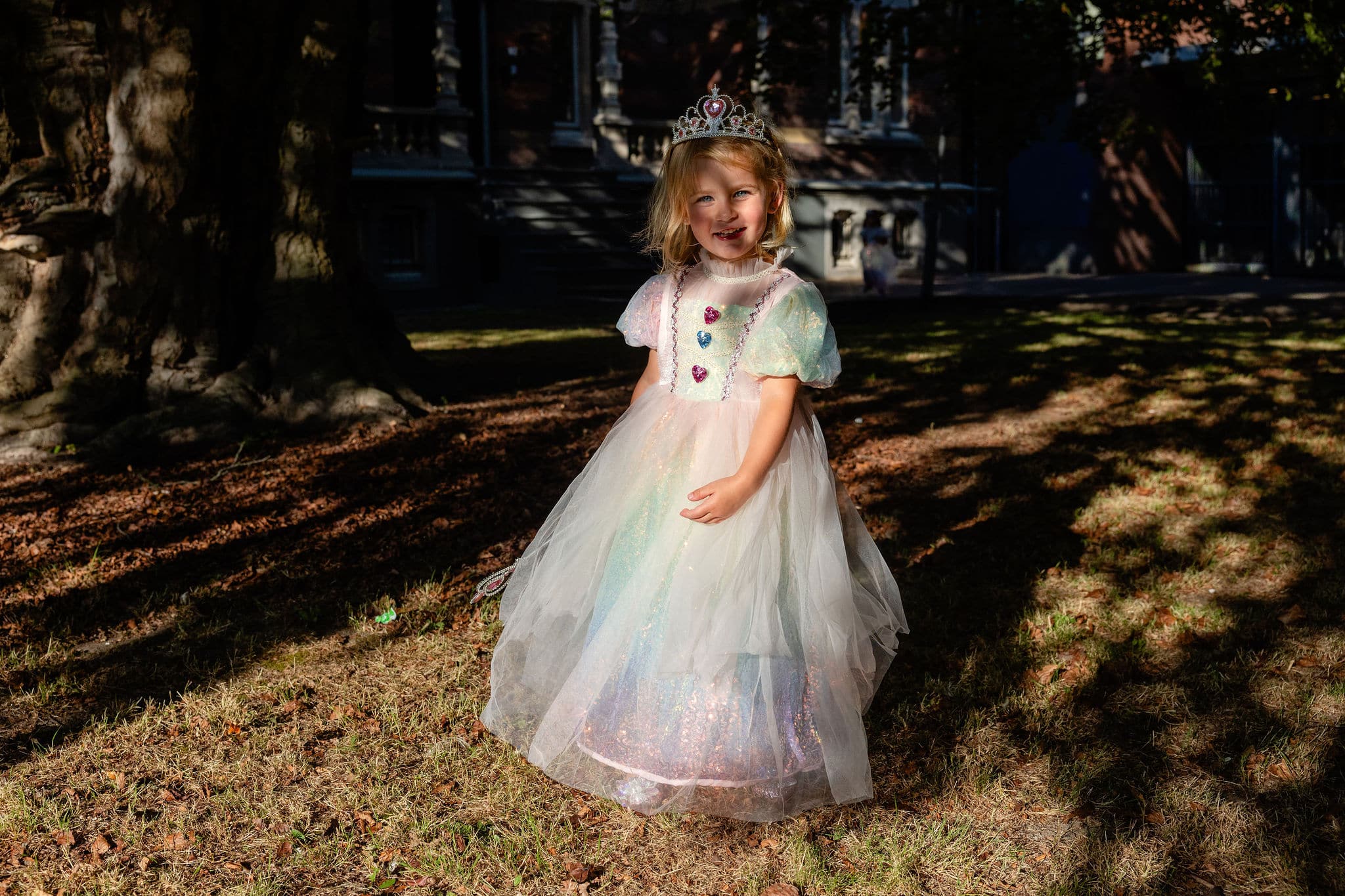 Meisje draagt een zachte regenboog prinsessenjurk met kroon en glanzende rok in een park