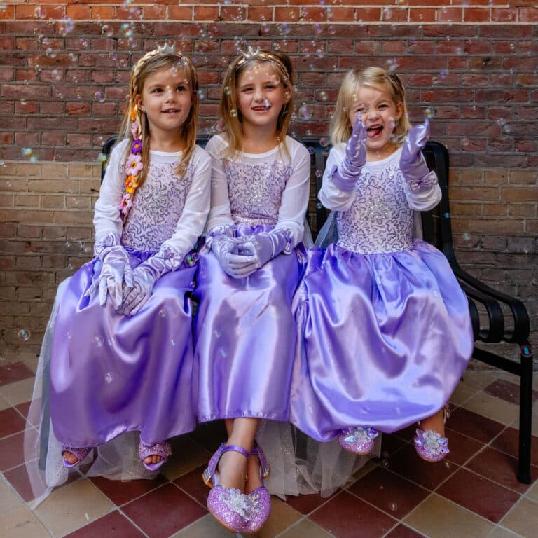 Drie meisjes dragen de paarse Elsa jurk met witte mouwen, lila handschoenen, tiara’s en glanzende lange rokken.
